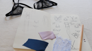 Design sketches and fabric samples on a notebook with black lace lingerie in the background.