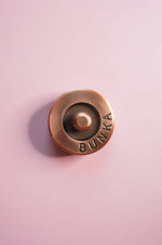 Bronze fabric weight with 'Bunka' engraving on a pink background